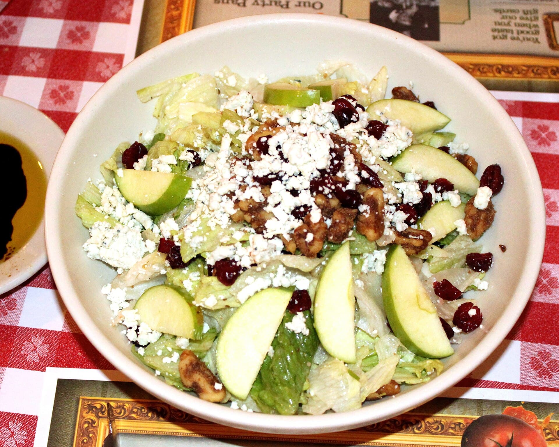 A bowl of lettuce salad with green apple slices, dried cranberries, walnuts and crumbled cheese.