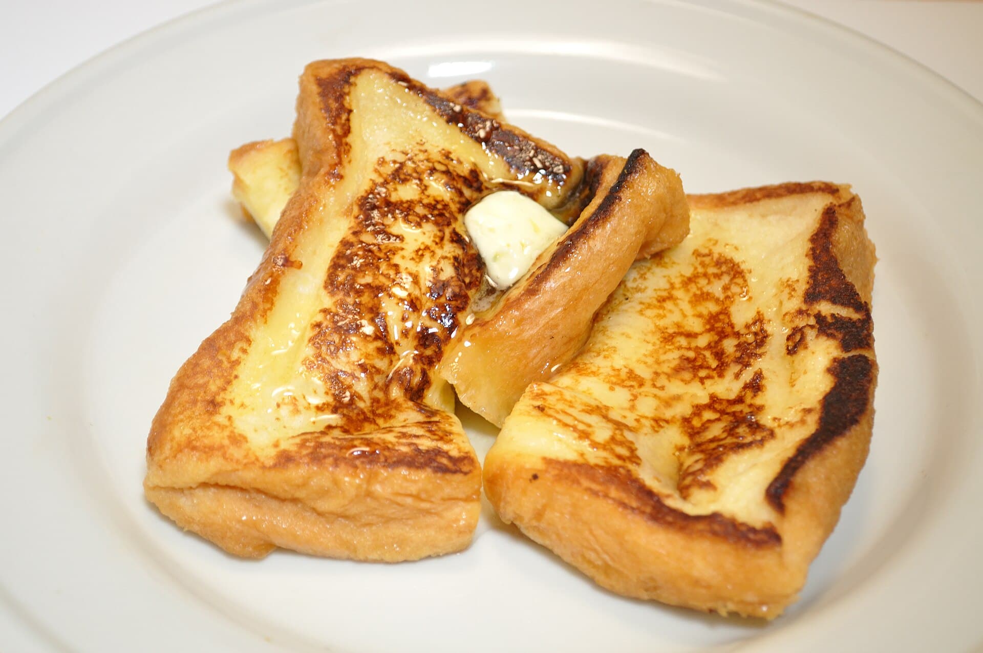Golden-brown slices of French toast topped with a pat of butter on a white plate.