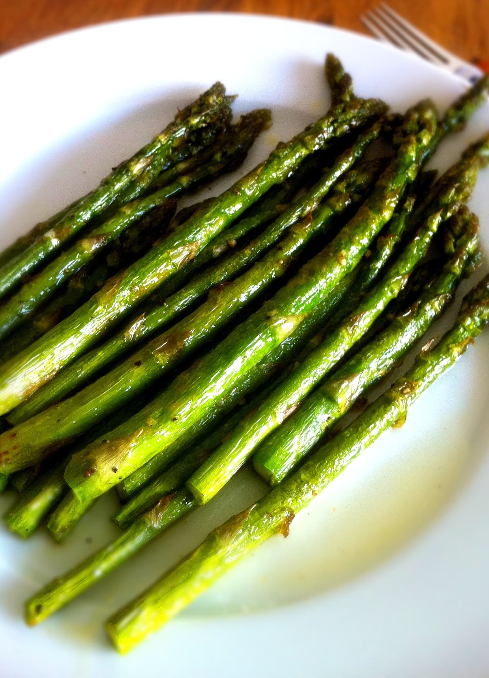A white plate of cooked green asparagus spears with a glossy finish.