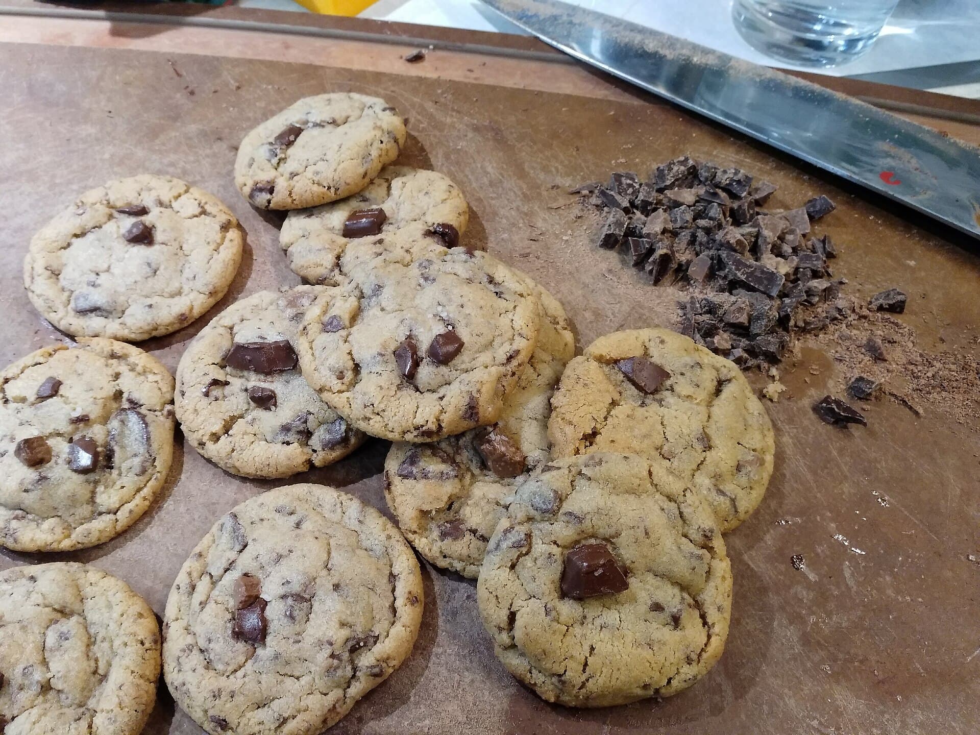Chocolate chip cookies scattered on a cutting board beside a small pile of chopped chocolate.