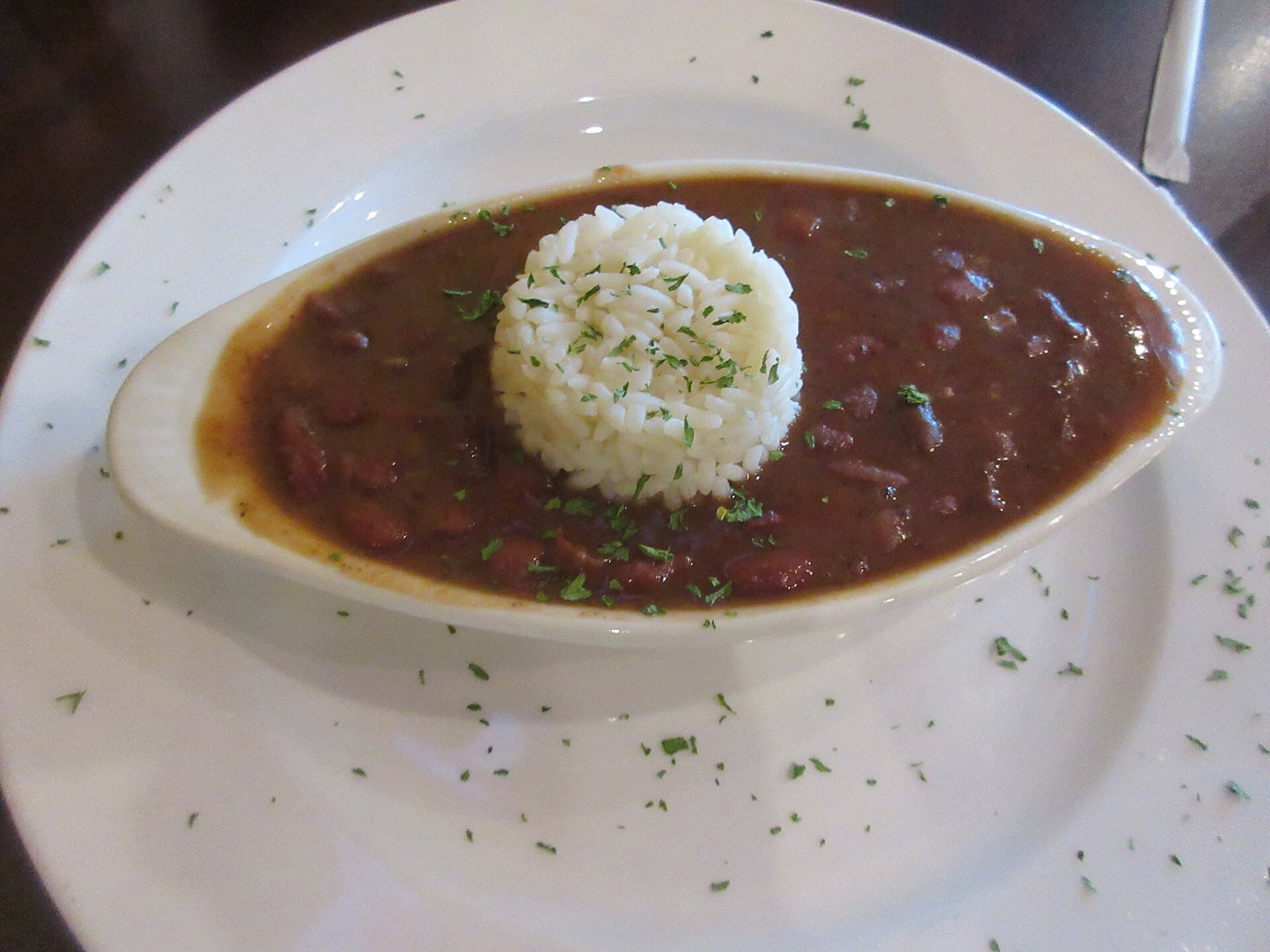 A dish of creamy red beans topped with a mound of white rice and a sprinkle of parsley.